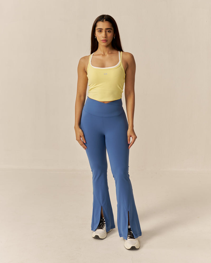 Woman wearing a yellow tank top and blue flared pants on a beige background