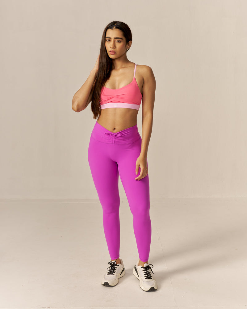 Woman wearing a two-toned pink sports bra and magenta pink leggings on a beige background