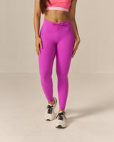 Woman wearing a two toned pink sports bra and magenta pink leggings on a beige background
