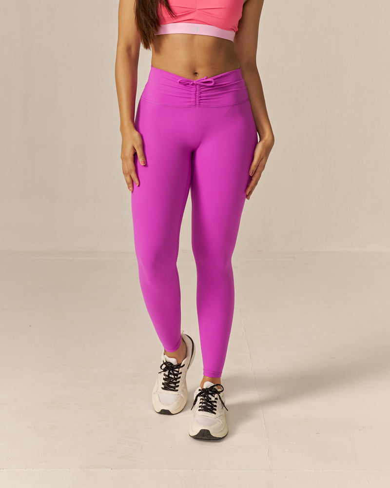 Woman wearing a two toned pink sports bra and magenta pink leggings on a beige background