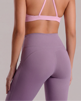 Person wearing a pink sports bra and purple leggings on a plain background