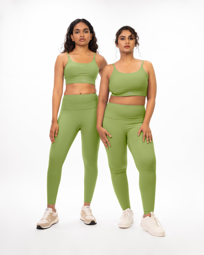An athletic female model with a plus size model posing in matching green sports bra and leggings suitable for gym and yoga, showcasing the coordinated activewear set on different body types. Model 1 is slim and athletic and model 2 is plus size