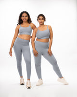 An athletic female model with a plus size model posing in matching grey sports bra and leggings suitable for gym and yoga, showcasing the coordinated activewear set on different body types. Model 1 is slim and athletic and model 2 is plus size