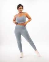 a plus size female model posing in a grey sports bra and matching leggings, showcasing the coordinated activewear set that is suitable for workout and daily wear