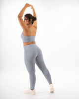 A plus size female model posing in a grey sports bra and leggings, showcasing the coordinated activewear set that is suitable for gym and yoga