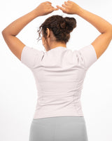 Female model showcasing the sleek back design of the pale grey Performance Tee, an ideal choice for intense workouts with its distraction-minimizing features.
