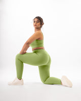 A plus size fit female model posing in a green sports bra and leggings, showcasing squat proof feature and the coordinated activewear set that is suitable for gym and yoga