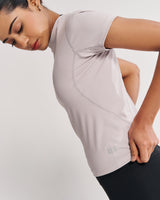 Athletic woman demonstrating the pale grey Performance Tee, a sweat-wicking gym top designed to provide maximum comfort and support during various fitness activities