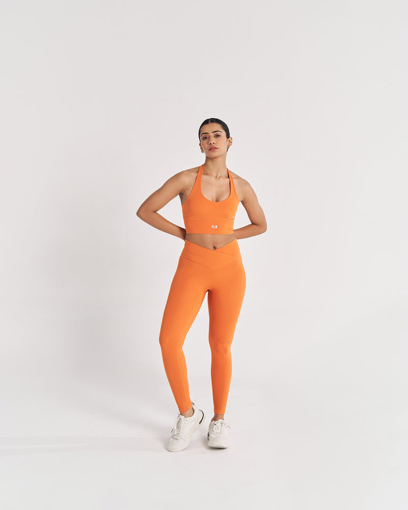female model in tangerine orange halter neck sports bra with matching leggings as co-ordinated set suitable for variety of athletic activities, gym, yoga and workout.