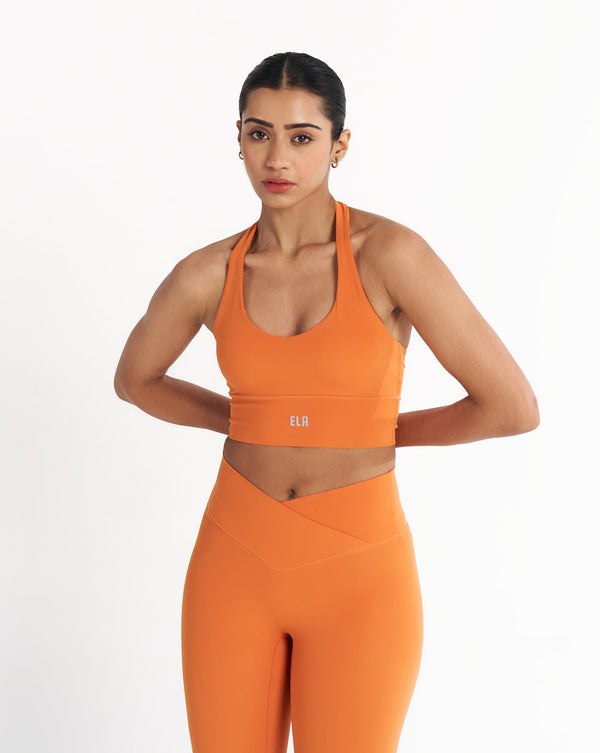Athletic woman in tangerine orange halter neck sports bra suitable for variety of athletic activities, gym, yoga and workout.