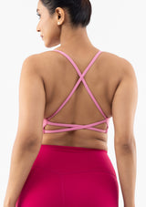 Rear view of a woman wearing a pink strappy sports bra and bright pink leggings against a clean white background.