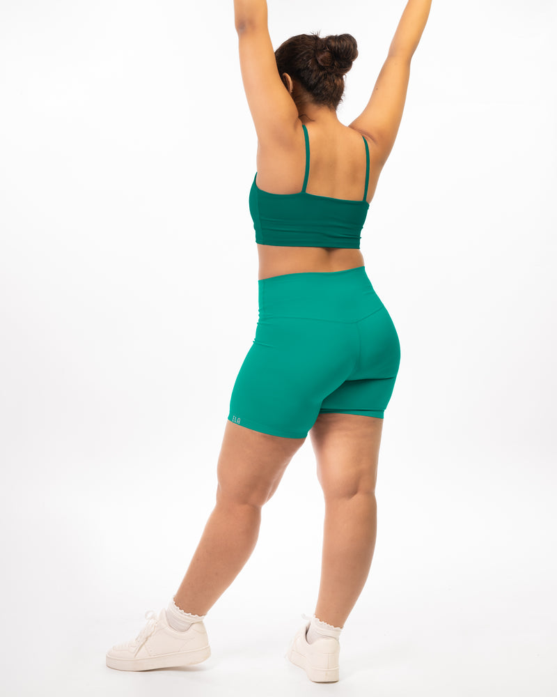 plus size Female model posing backwards in premium green high waisted and squat proof bike shorts suitable for athletic activities with dark green sports bra giving a monochromatic athleisure look