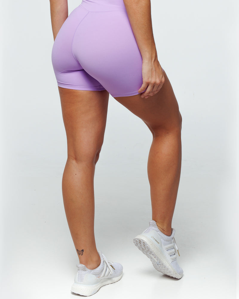female athletic model wearing buttery smooth lilac bike shorts perfect for running, biking and daily life. The high waistband shows the criss cross feature with wrapover waistline and shows squat proof feature.