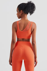 Female model posing to display orange buttery smooth leggings with a high waist and ankle-length fit with a matching sports bra suitable for gym, yoga and other athletic activities