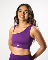 Model wearing a purple one shoulder strap sports bra with an optional detachable second strap, suitable for a variety of workout activities.