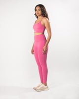 Model posing in pink activewear set including a sports bra and gym leggings, perfect for any workout or athletic activity.