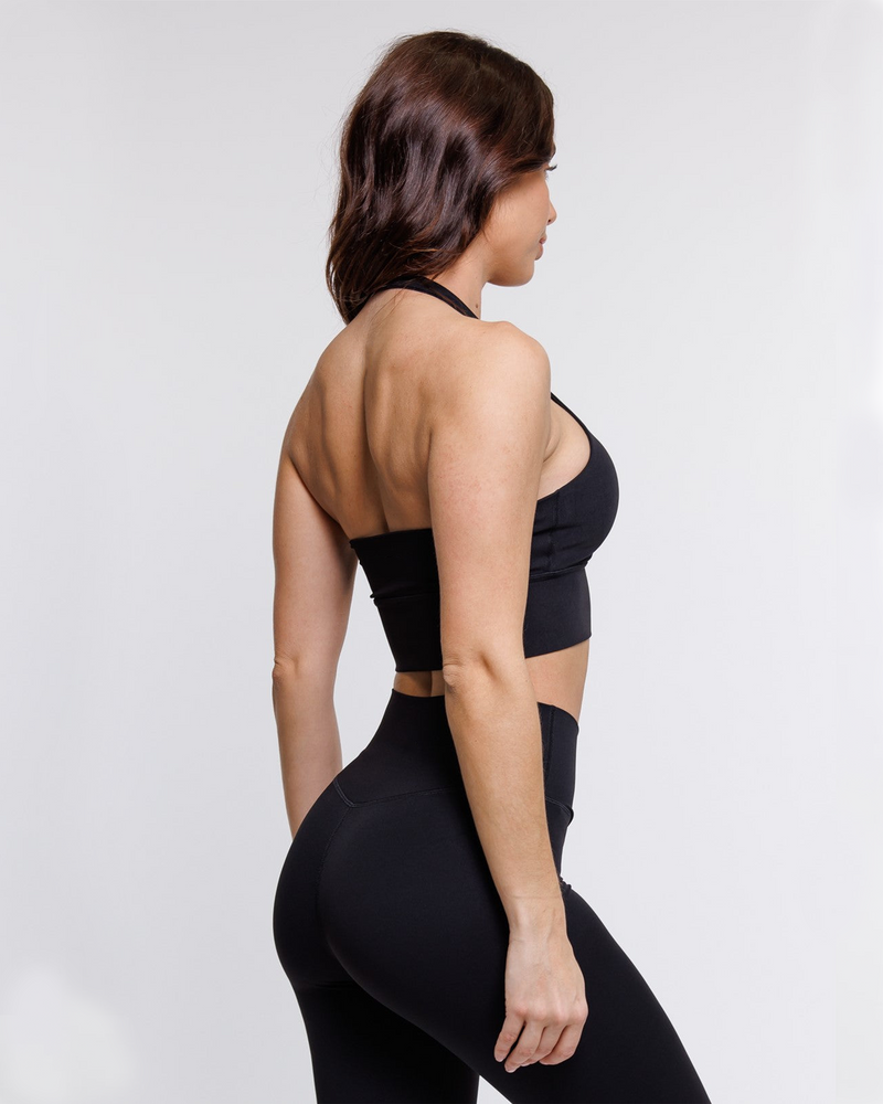 female model showing flattering back design of black halter neck sports bra with matching leggings suitable for variety of athletic activities, gym, yoga and workout.