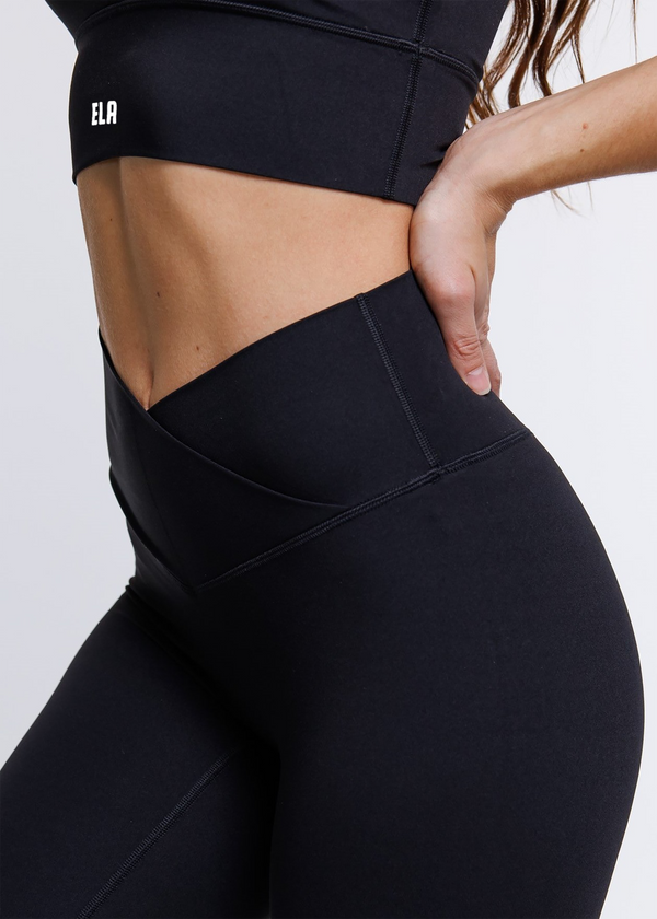 A female model wearing the ButterBod Hourglass Leggings, highlighting close up of legging. The high-waisted wrap design and V-cut waistband accentuate her curves, while the booty-lifting back seam provides a flattering lift. The leggings have a soft matte finish, medium compression, and are made from 4-way stretch fabric for maximum comfort and versatility.