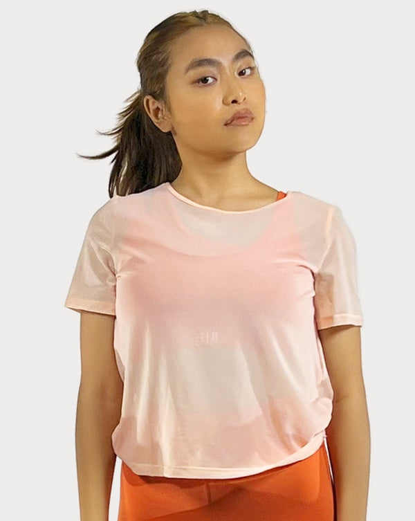 Female model is showing the orange gym tee that has a round scoop neck in the front made of fine mesh fabric with a flattering V-shaped twisted open back design. The top is perfect for use as a cover-up on top of a sports bra and is great for gym, yoga, or everyday wear. 