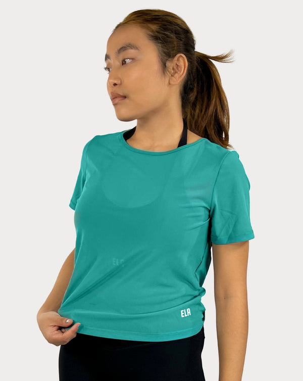 Female model is showing the green gym tee that has a round scoop neck in the front made of fine mesh fabric with a flattering V-shaped twisted open back design. The top is perfect for use as a cover-up on top of a sports bra and is great for gym, yoga, or everyday wear. 